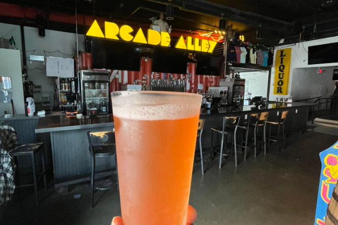 image of a glass of beer with a neon arcade alley sign in the background